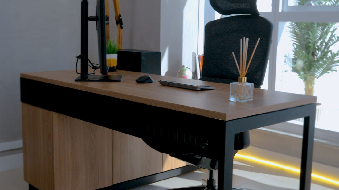 Imagem mostra a mesa Bernardi da Elements montada em um ambiente de escritório. Tem um monitor, teclado e mouse sobre ela e uma cadeira ergonômica ao lado.